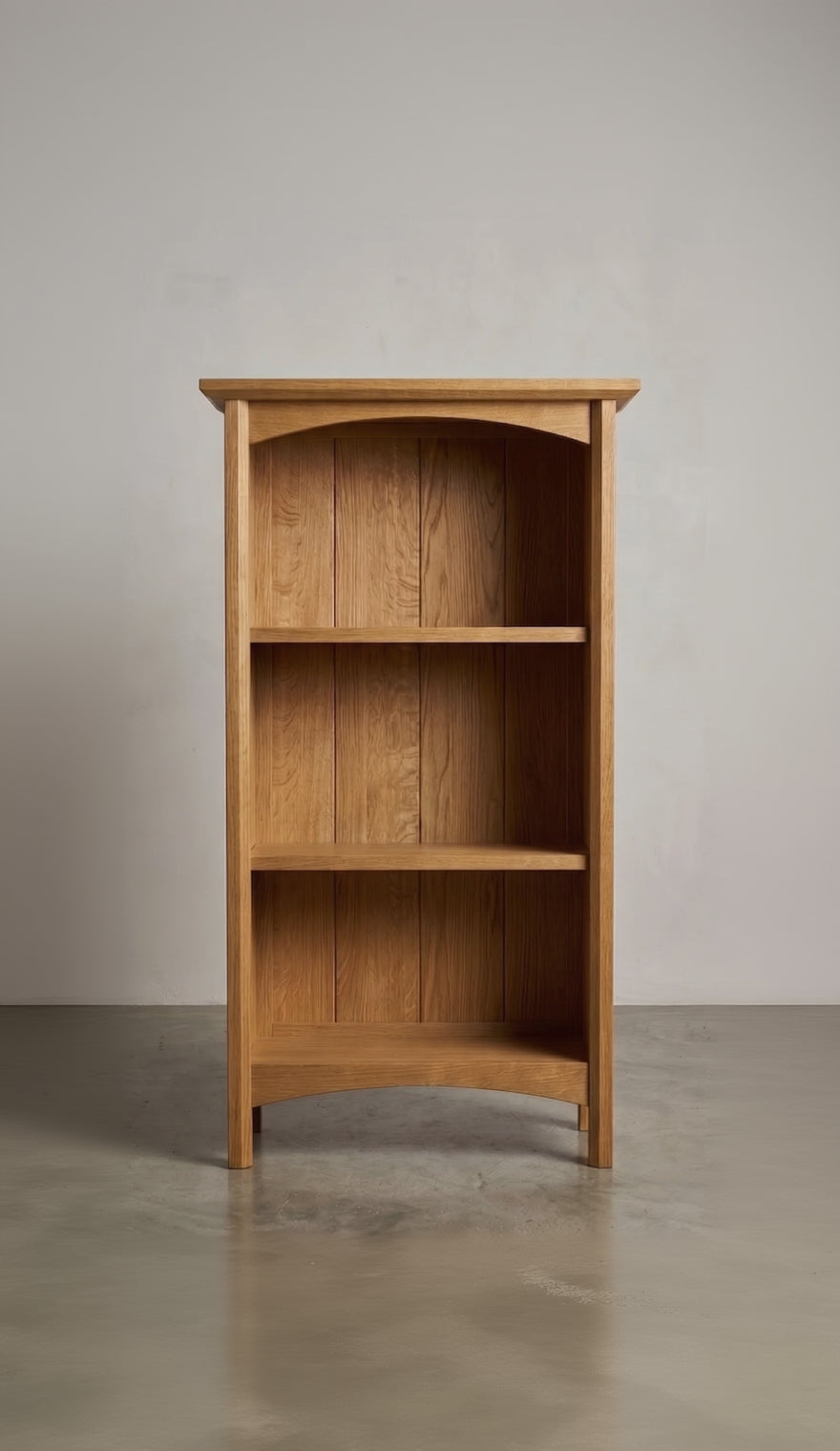 Wooden oak bookshelf with three shelves against a plain wall.