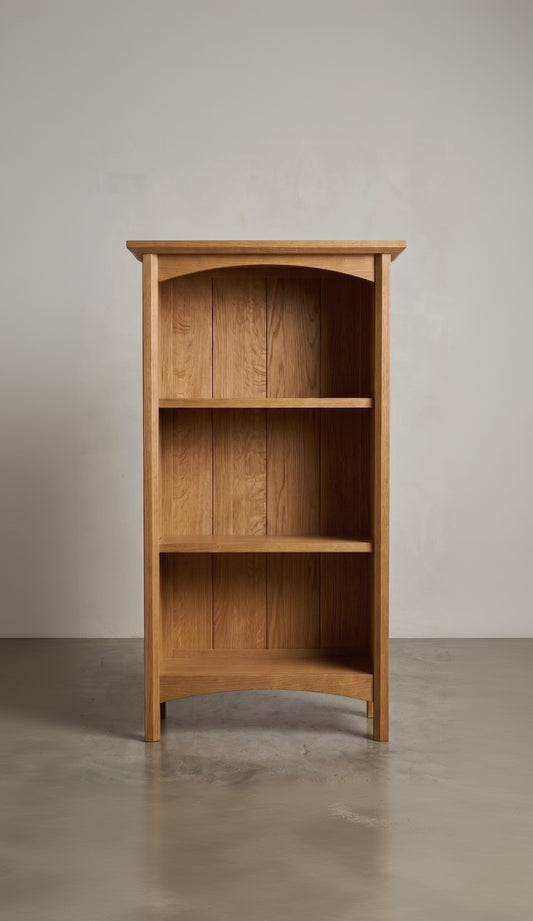 Wooden oak bookshelf with three shelves against a plain wall.