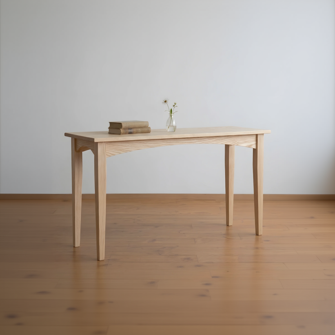 Wooden table with a vase and books on a wooden floor against a white wall
